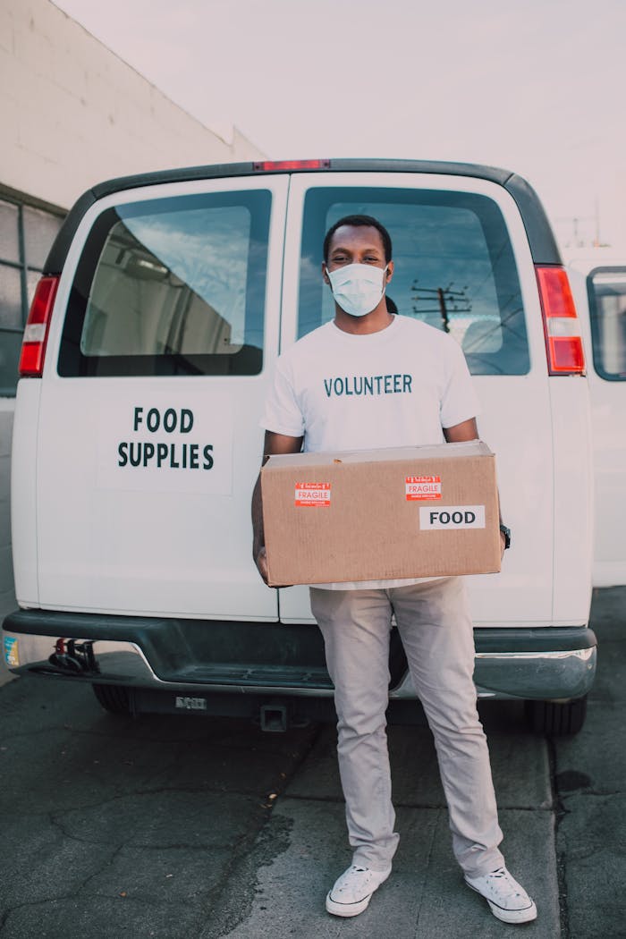 A masked volunteer delivering food supplies from a van to support pandemic relief efforts.