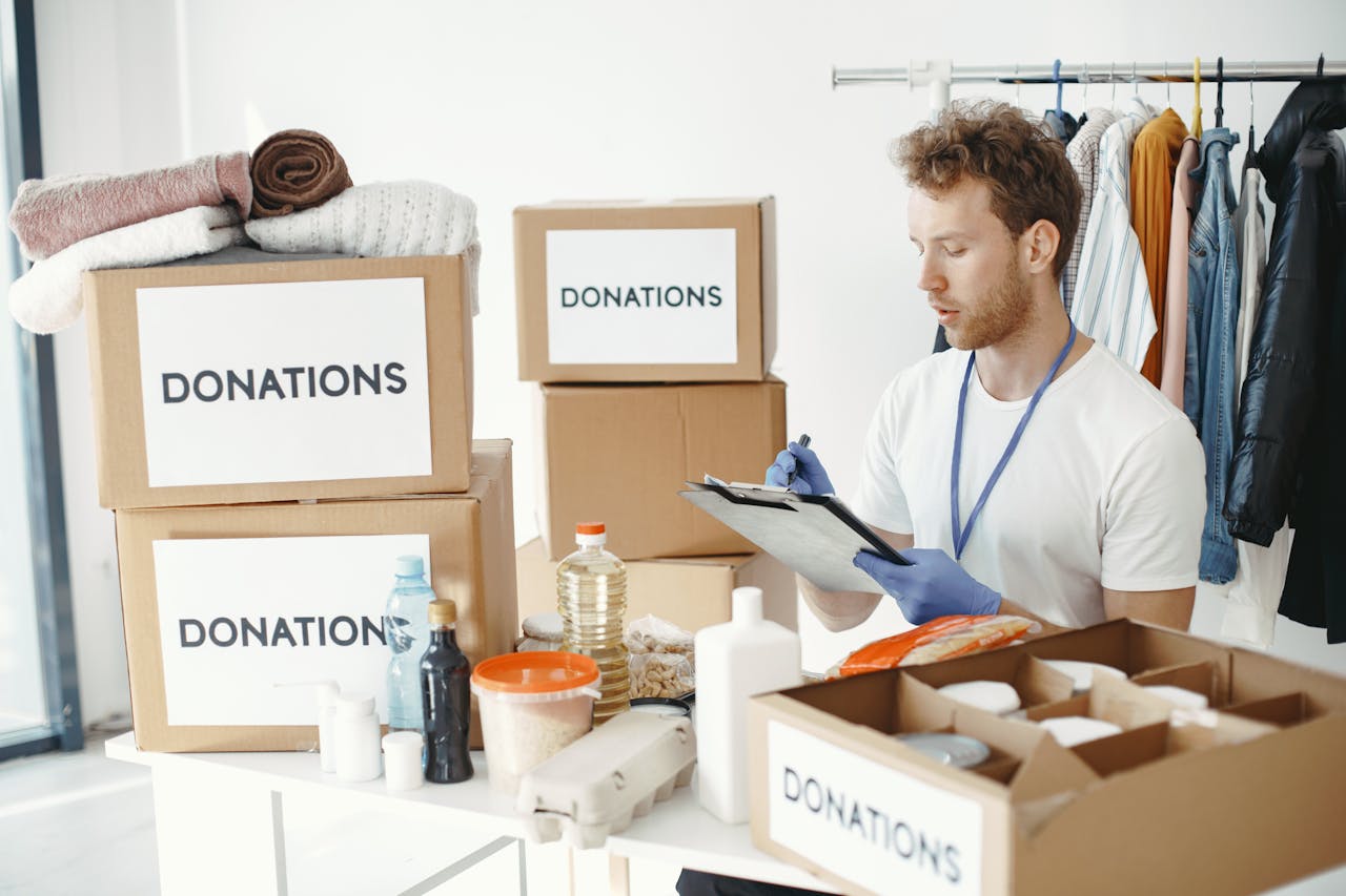 A man organizing donation boxes filled with clothes and food items at an NGO office.