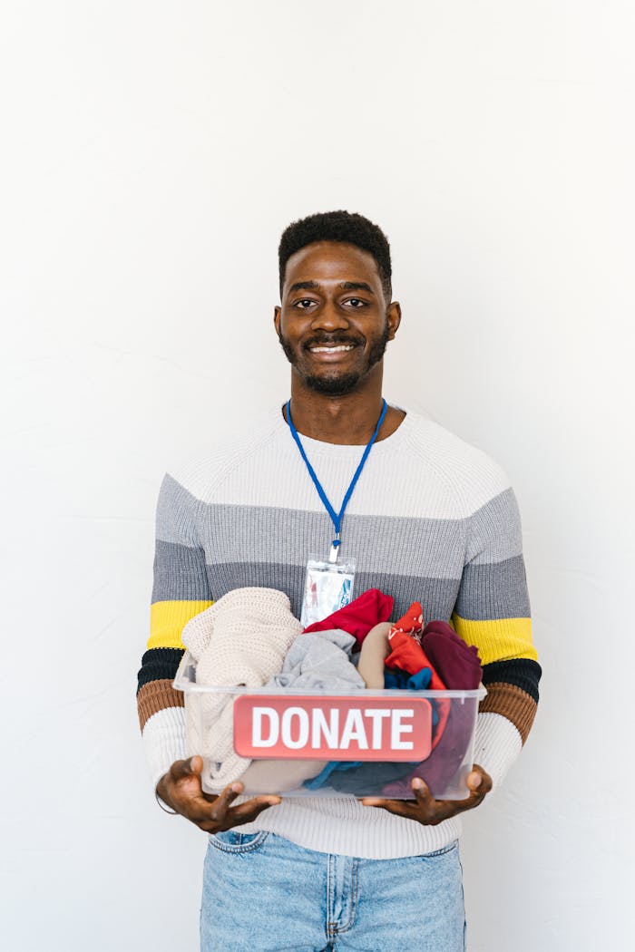 A smiling man holds a clear box full of clothing donations against a white background.