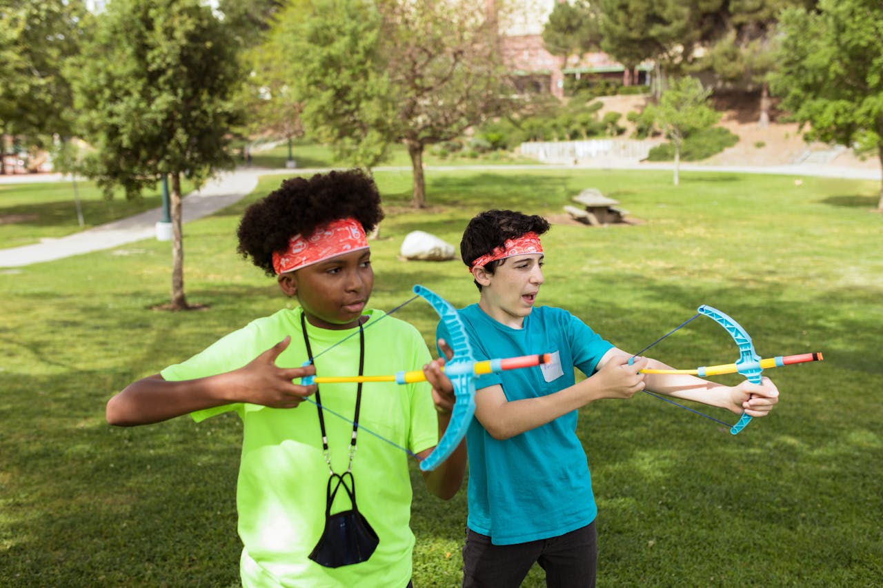 Two children practicing archery outdoors, having fun and learning teamwork at summer camp.